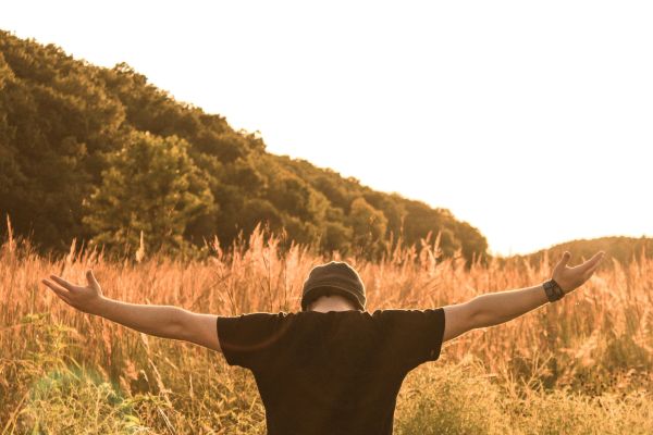 a man in a field with a black shirt on with his hands lifted displaying his lifestyle of worship
