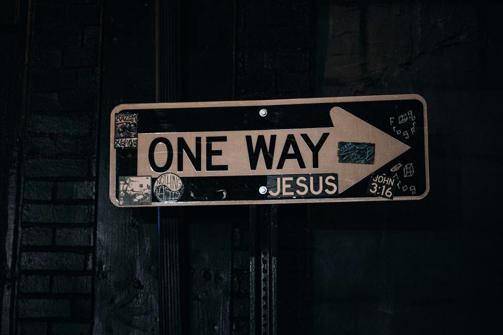 a street sign with a white "one way" arrow and "Jesus" imprinted underneath the arrow