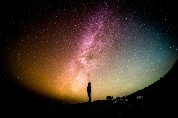 a silhouette of a person standing under the stars of the sky which illustrate the awesomeness of god