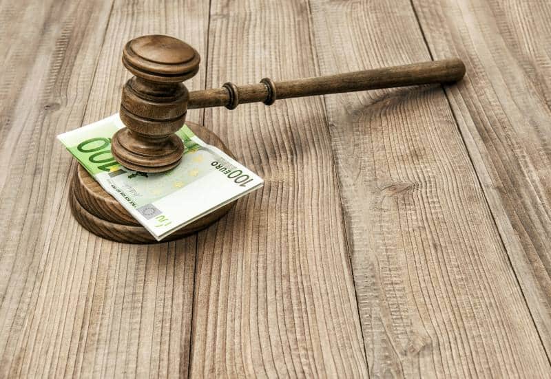a gavel with a 100 euro of paper money in between it laying on a wooden desk