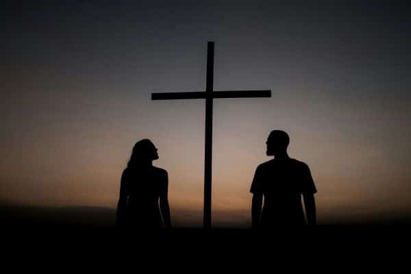 a man and a woman silhouette with a cross in the background and a colorful sky behind it illustrating the power of prayer